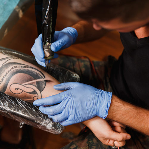 close-up-of-professional-tattooer-artist-doing-tattoo-on-the-arm-of-young-man-by-machine-with-black-ink
